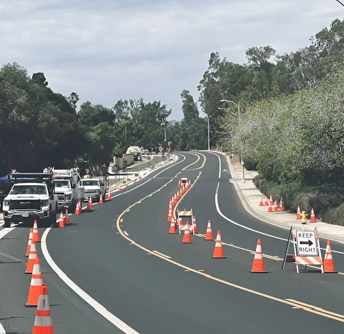 A road with orange cones blocking off the side of it.